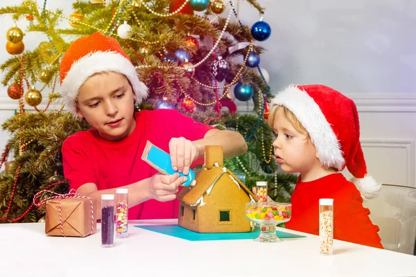 Two Happy Boy Santa Hat Build Gingerbread House Gluing Candies — Fotografia de Stock