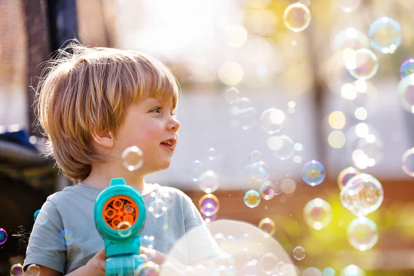 Close portrait of a cute boy play with soap bubbles holding bubble gun it the playground