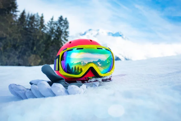 Pink sport helmet with ski mask and winter gloves in snow over mountain range on background