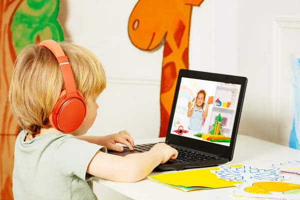 Cute little blond boy watch education videos over internet on laptop wearing headphones