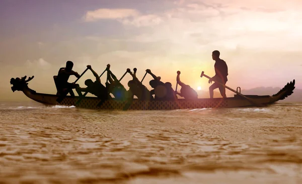 Silhouette of a Dragon boat with people paddling at sunset