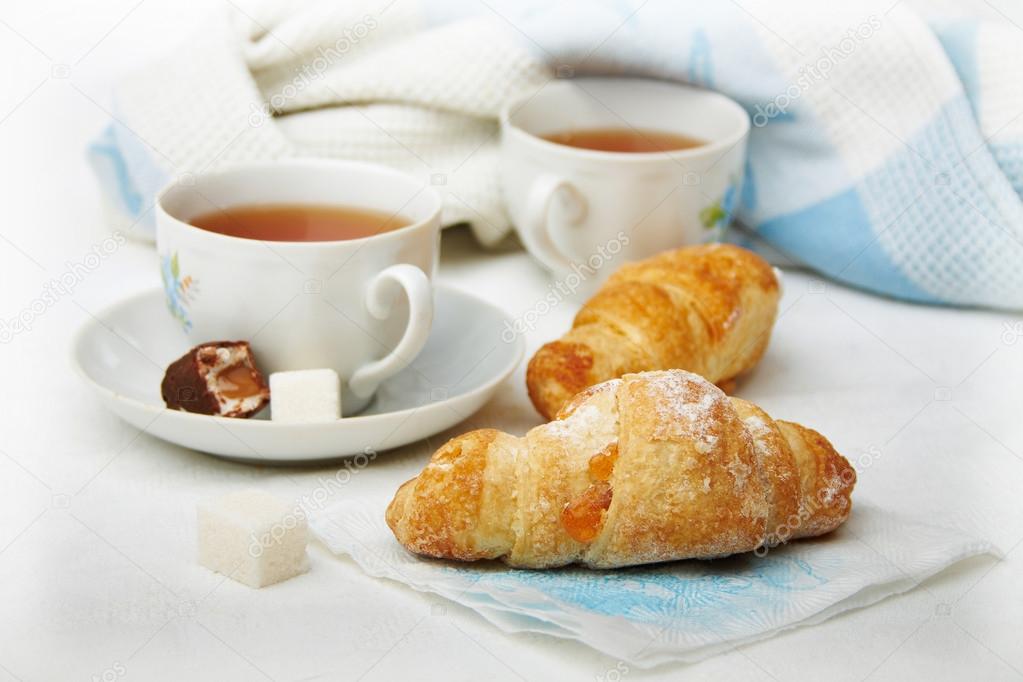 Two cups of tea with croissants on the desktop, a white-blue ton
