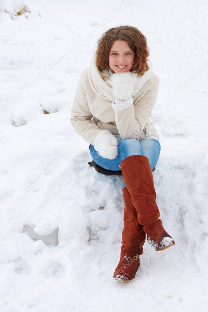 The pretty girl smiles in the camera, sitting on snow