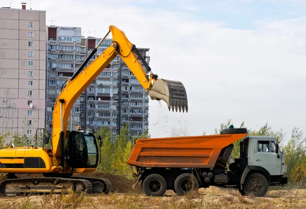 Graafmachine laadt de grond in een vrachtwagen op een achtergrond van huizen — Stockfoto