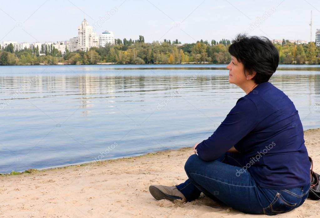 Woman sitting on the sand by the river