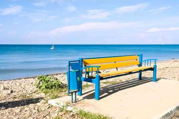 Bänk på stranden av det blå havet — Stockfoto