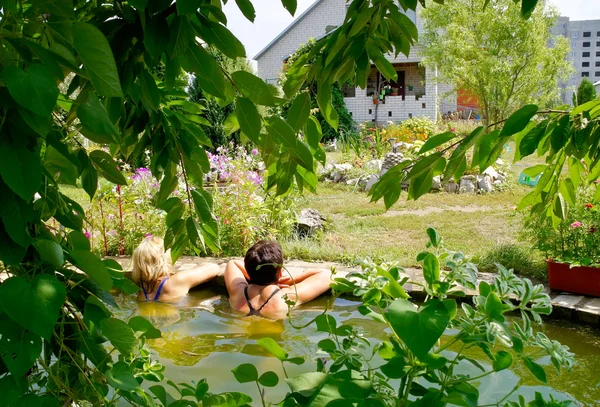 Twee vrouwen zwemmen in het zwembad bij hun zomerhuisje. — Stockfoto