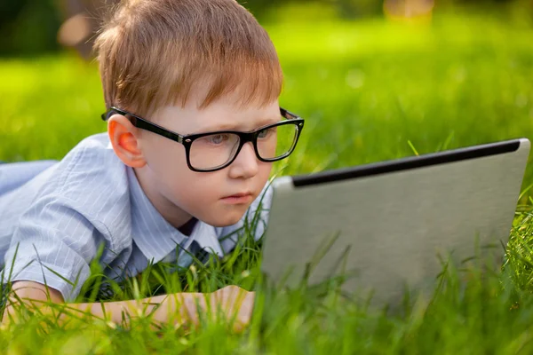 Menino deitado na grama no parque com laptop — Fotografia de Stock