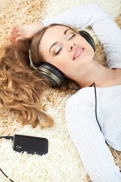 Femme couchée sur le tapis et écoutant de la musique Photo De Stock