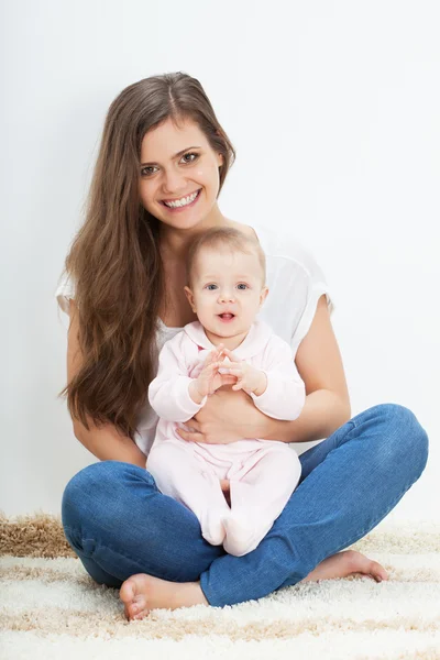 Jonge moeder en baby zittend op tapijt Stockfoto