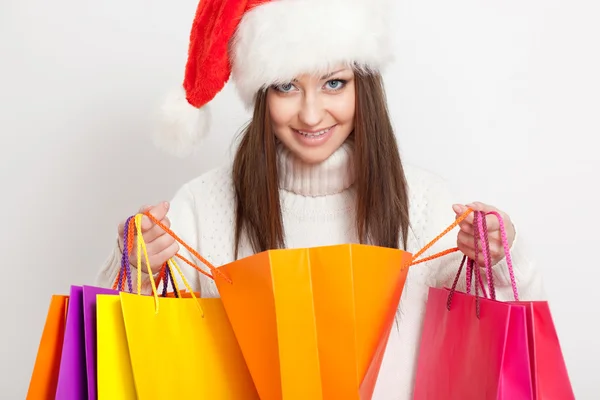 Brunette vrouw in Kerstman hoed, bedrijf shopping tassen — Stockfoto