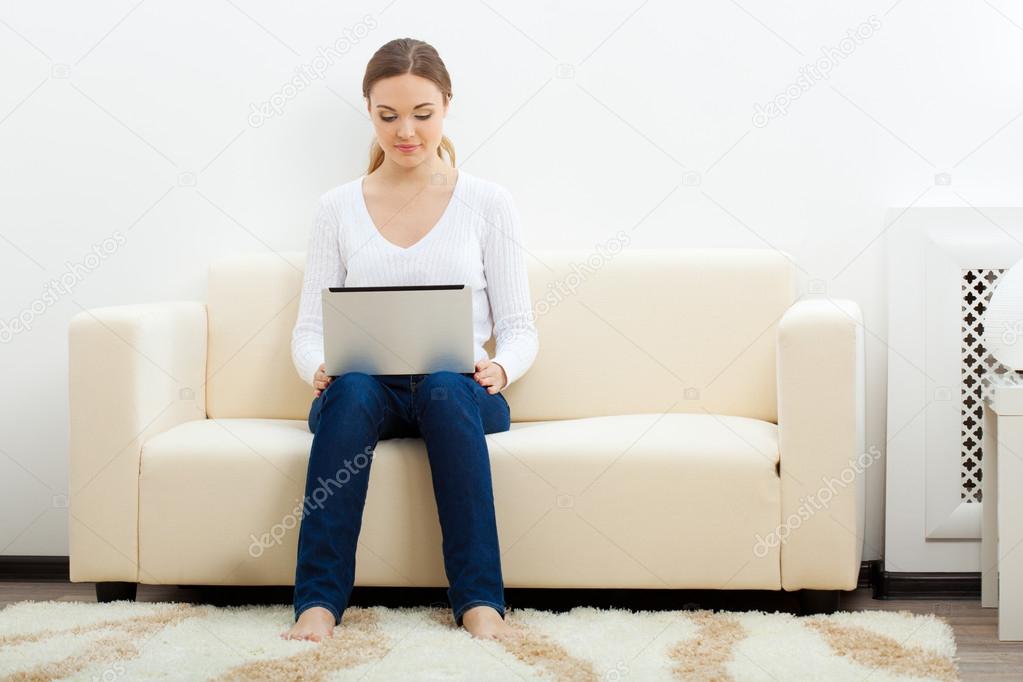 Happy woman sitting on sofa with laptop
