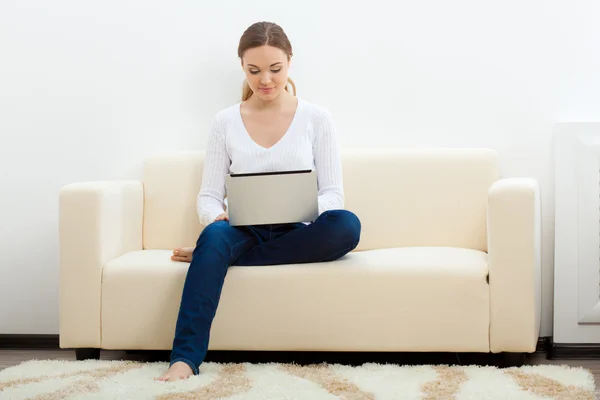 Счастливая женщина сидит на диване с ноутбуком — стоковое фото