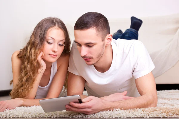 Couple lying on carpet and looking at tablet Stock Image