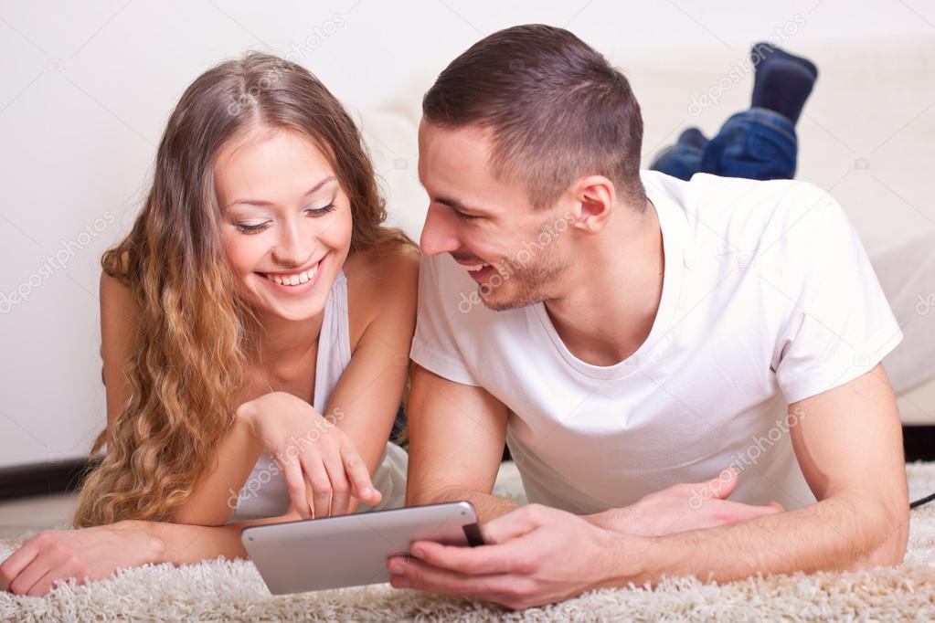 Couple lying on carpet and looking at tablet