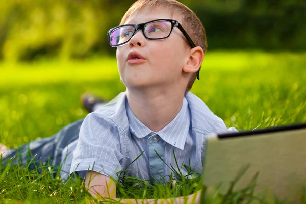 滑稽的男孩躺在公园的笔记本电脑的草地上 — 图库照片
