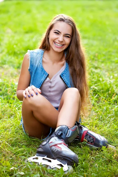 Lány visel görkorcsolya ül a fűben — Stock Fotó