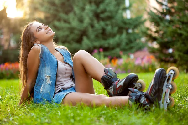 Flickan bär rullskridskor sitter på gräset — Stockfoto