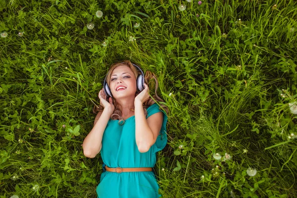 Mujer acostada en la hierba con auriculares — Foto de Stock