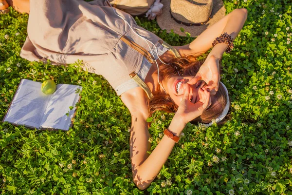 Kvinna som bär hörlurar liggande på gräs — Stockfoto