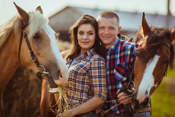 Casal em pé na fazenda com cavalos — Fotografia de Stock