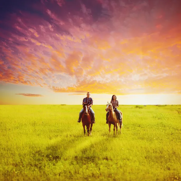 Copule chevauchant sur des chevaux au coucher du soleil — Photo