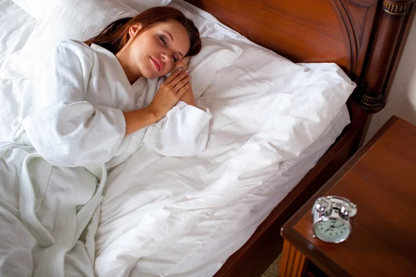 Kvinna i sängen att utvidga hand till väckarklockaスマート フォンを使用して幸せなカジュアルな若い女 — Stockfoto