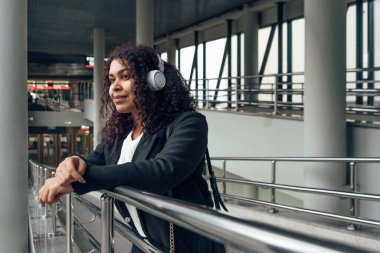 Geçiş bölgesinde, kulaklık takıp pencereye bakan genç bir kadın.