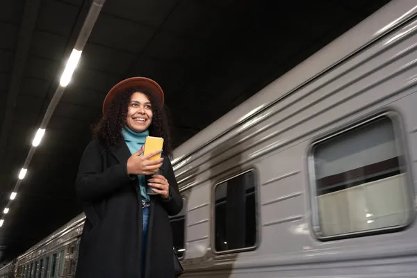 電車の前に立ってコーヒーや電話を持って横を見る女性 — ストック写真