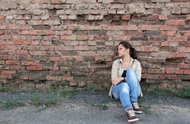 bir tuğla duvara oturan üzgün genç kız