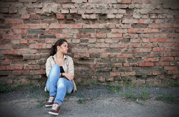 Sad young girl sitting against a brick wall — Stock Photo, Image