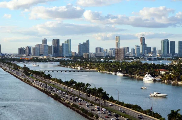 Panoramic view from an upper deck of an outward bound  cruise ship of Government Cut,eastbound bumper to bumper. traffic on the MacArthur Causeway , luxury motor yachts moored at Hibiscus Island,Miami Beach and Miami\'s tall building skyline .