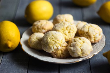 Limon meyveli, gri ahşap arka planda beyaz bir tabakta yuvarlak limonlu kurabiyeler. Ev yapımı kurabiye.