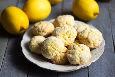 Limon meyveli, gri ahşap arka planda beyaz bir tabakta yuvarlak limonlu kurabiyeler. Ev yapımı kurabiye.