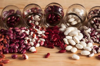 Multi-colored beans are poured out of jars on the table. White, red and colored beans. Background clipart