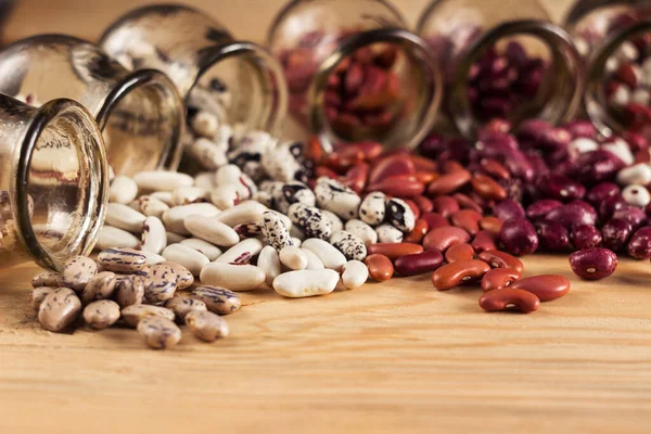 テーブルの上のガラス瓶から注ぐ多色の豆 — ストック写真
