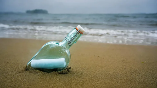 Bottle on beach with message on paper inside in rainy day