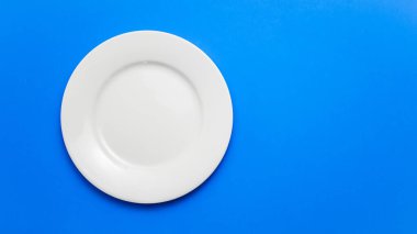 Empty white plate on blue background with copy space