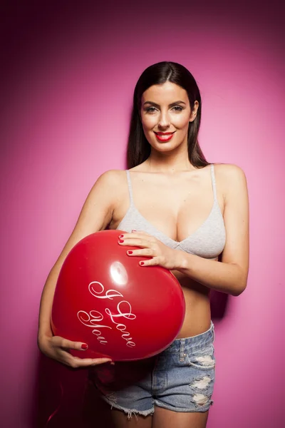 Sexy bruneta žena s valentines den balónky na růžovém pozadí — Stock fotografie