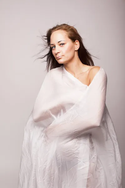 Sexy brünette Frau mit perfektem Körper mit weißen transparenten Textilien auf grauem isolierten Hintergrund bedeckt — Stockfoto