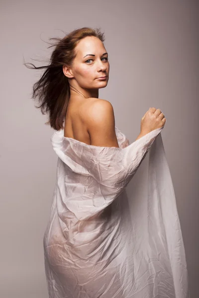 Mujer morena atractiva con cuerpo perfecto cubierto con textil transparente blanco sobre fondo aislado gris —  Fotos de Stock
