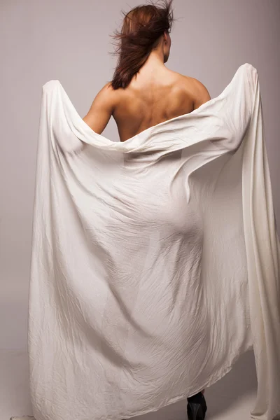 Sexy brünette Frau mit perfektem Körper mit weißen transparenten Textilien auf grauem isolierten Hintergrund bedeckt Stockbild
