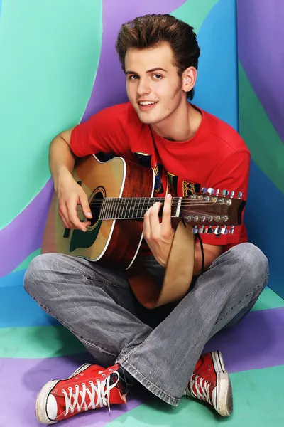 Handsome happy boy is playing on acoustic guitar on a colored ba — Stock Photo, Image
