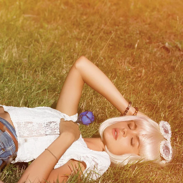 Den vackra blondin med blå ros i handen liggande på gra — Stockfoto