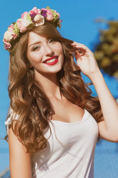 Beautiful brunette with long curly hair in a wreath of flowers — Stock Photo, Image