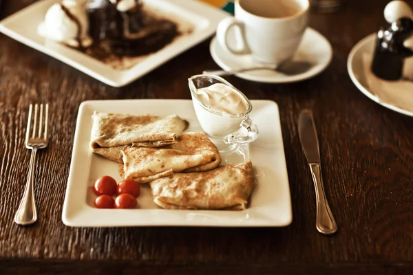 Pancakes on plate with condensed milk and tomato on table — Stock Photo, Image