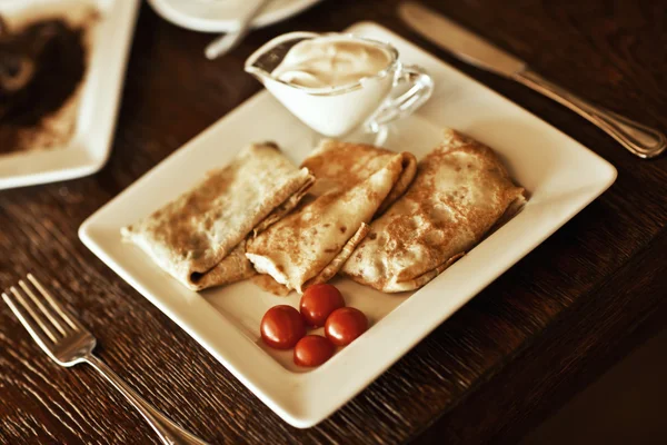 Tortitas en plato con leche condensada y tomate en la mesa —  Fotos de Stock