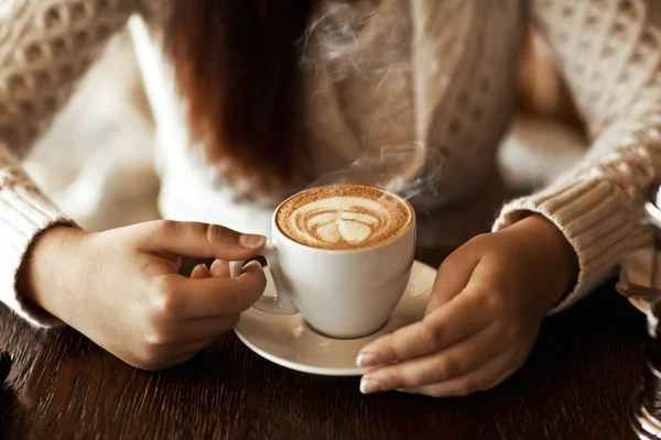 Mãos de mulher com latte em uma mesa de madeira Imagens Royalty-Free