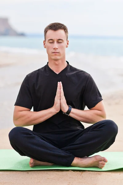 Genç adam plajda yoga yapıyor.