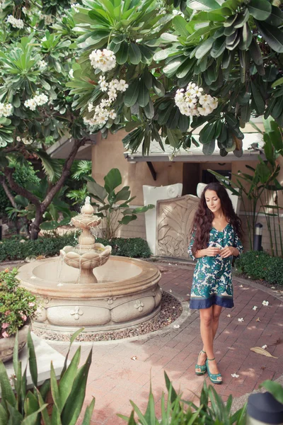 Docela usměvavá brunetka v květované šaty pózuje u fontány — Stock fotografie